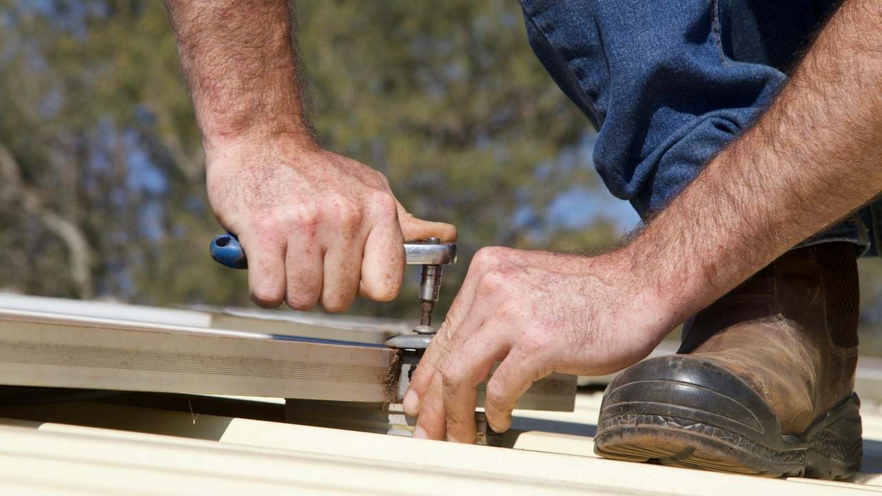 Montatori profesioniști executând prinderile precise ale învelitorii de acoperiș