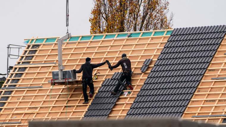 Montatori Calonix așezând țiglă metalică neagră pe un acoperiș nou cu șipci