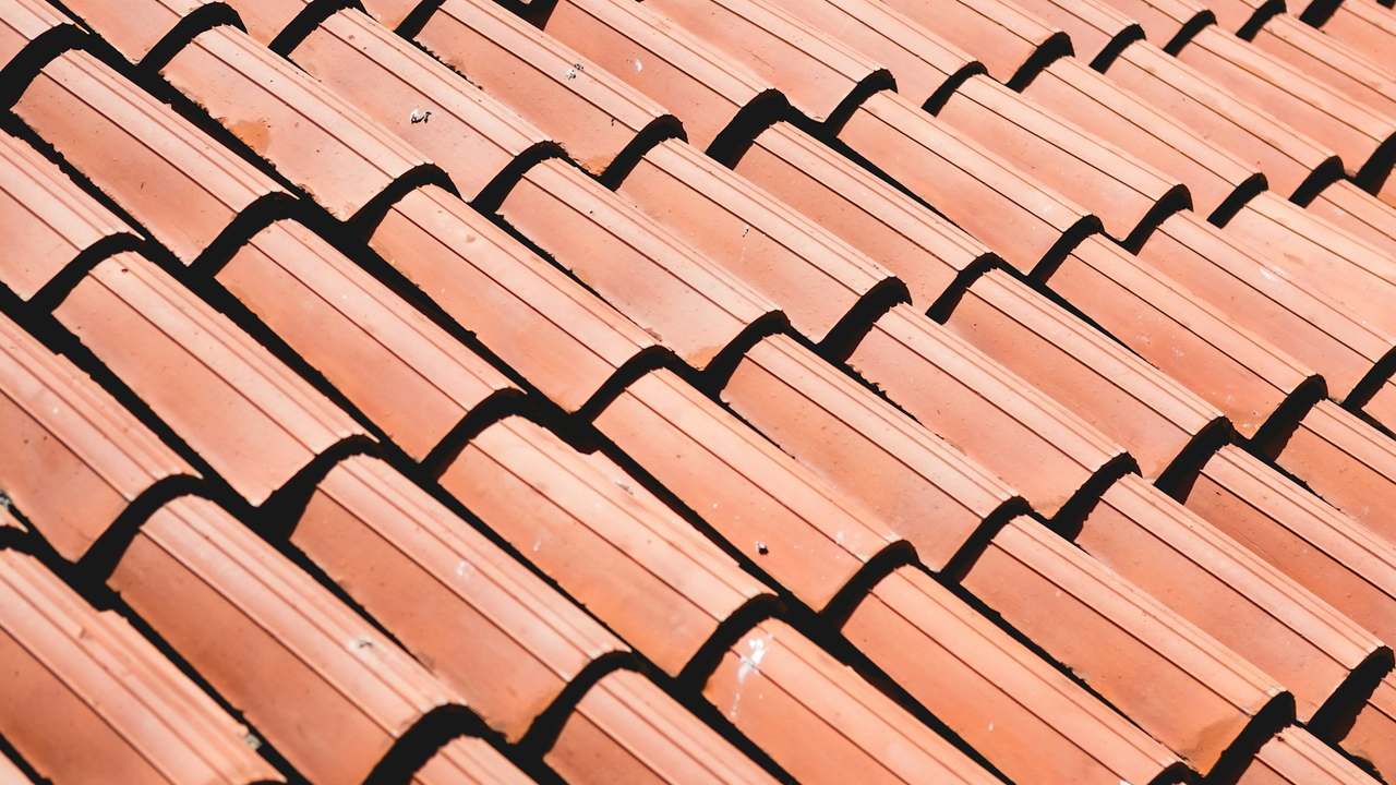 Palet cu țigle ceramice premium și montator verificând alinierea pe șipci