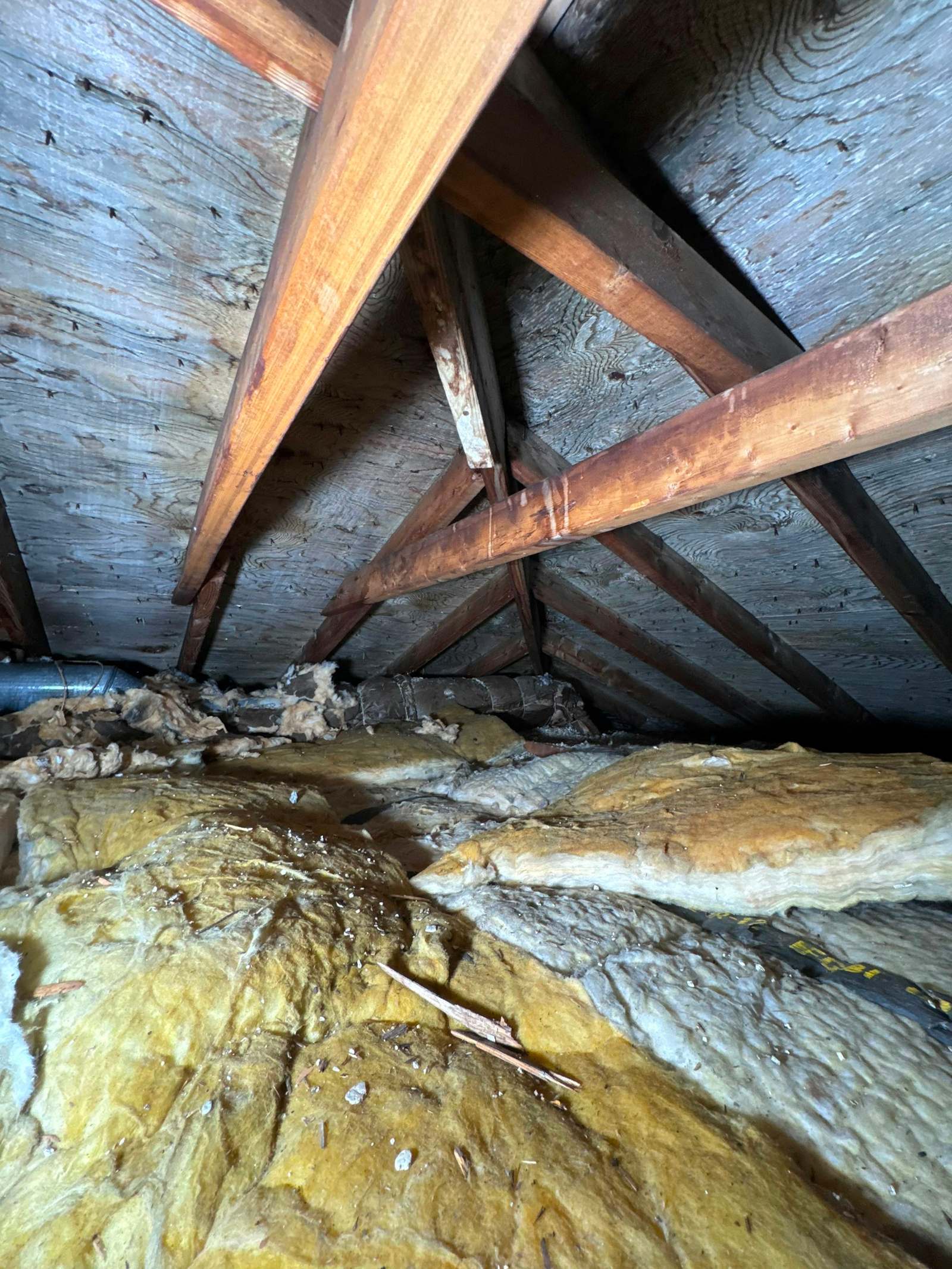 Vată minerală galbenă montată între căpriorii din lemn ai unui pod